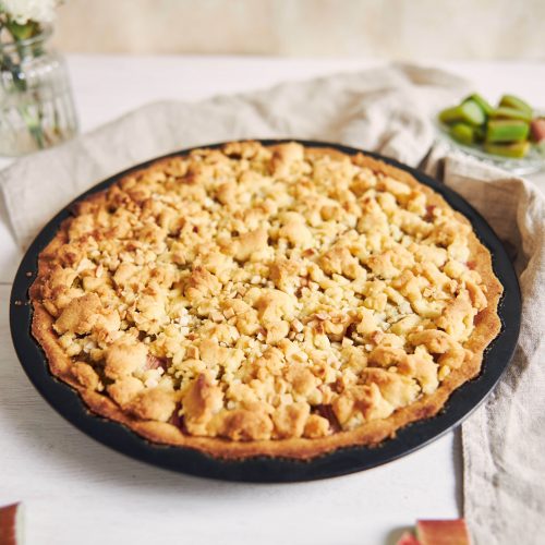 A vertical high angle shot of a plate of crispy Rhabarbar cake tart and some ingredients on a table