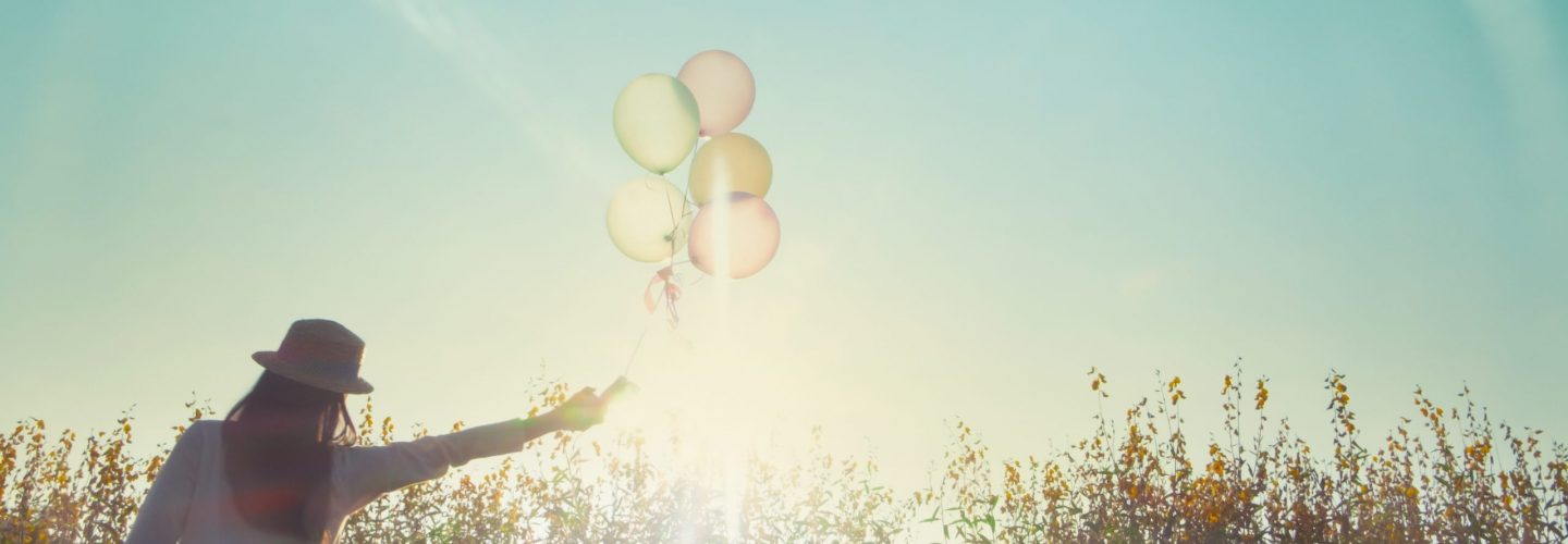 Girl running on the field of yellow flowerwith balloons at sunset. Happy woman on nature, concept about carefree airiness and relax, vintage effect.